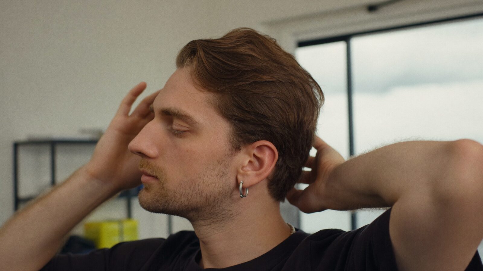 Man running his hands through his hair at the temples in a bright room