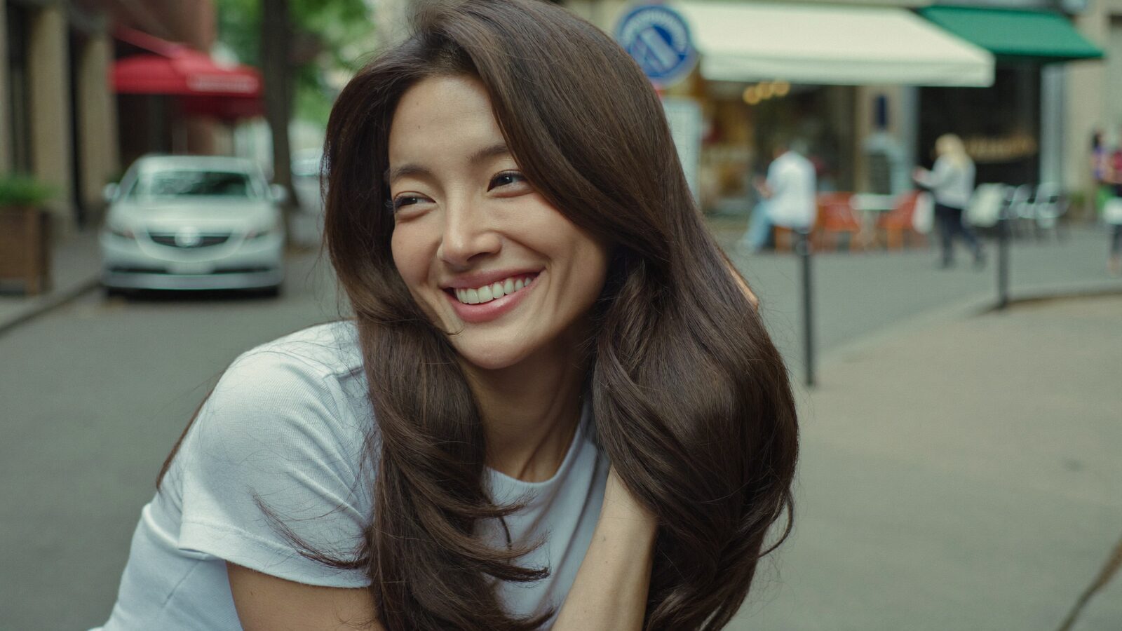 Smiling woman with long, softly layered dark hair on a city street