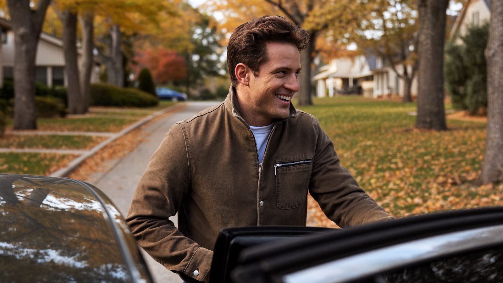 Smiling man with full dark hair opening his car door on a tree-lined suburban street in autumn