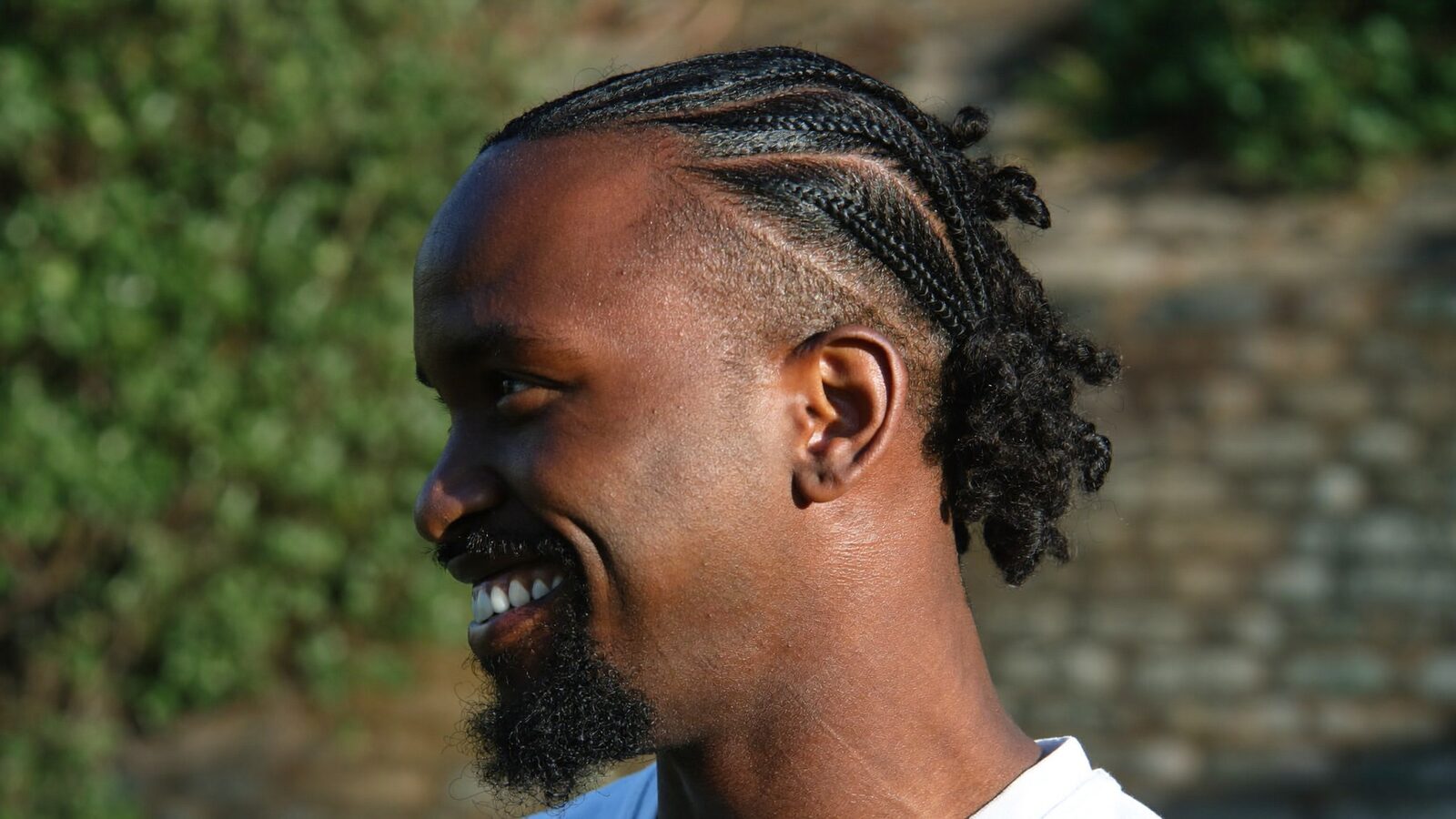 Smiling man with braided natural hair outdoors in warm light