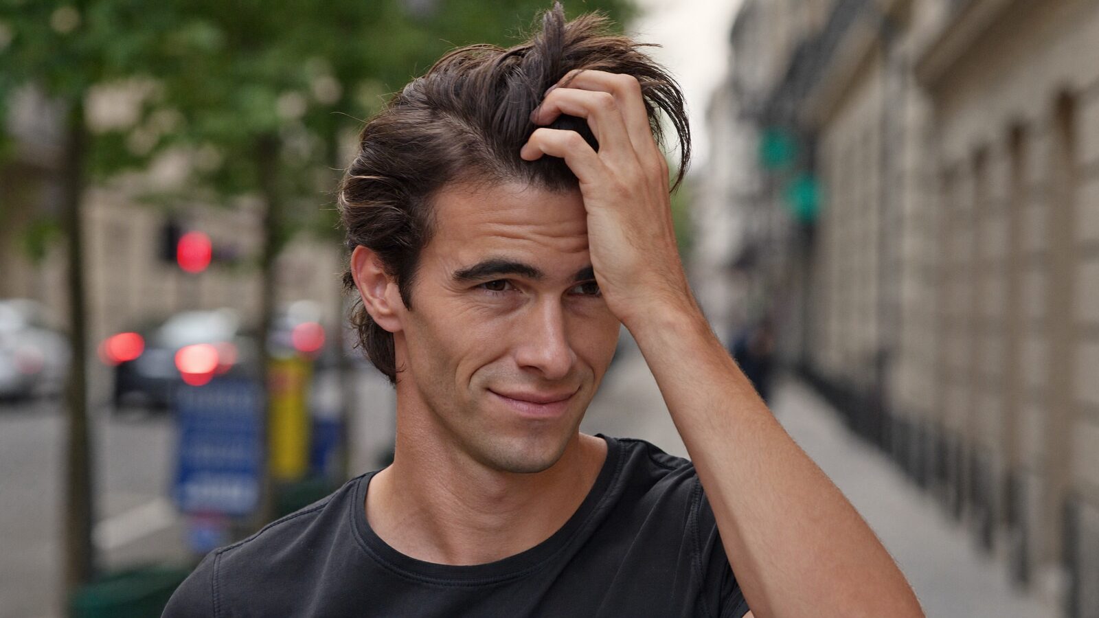 Man running a hand through thick, healthy hair on a city street