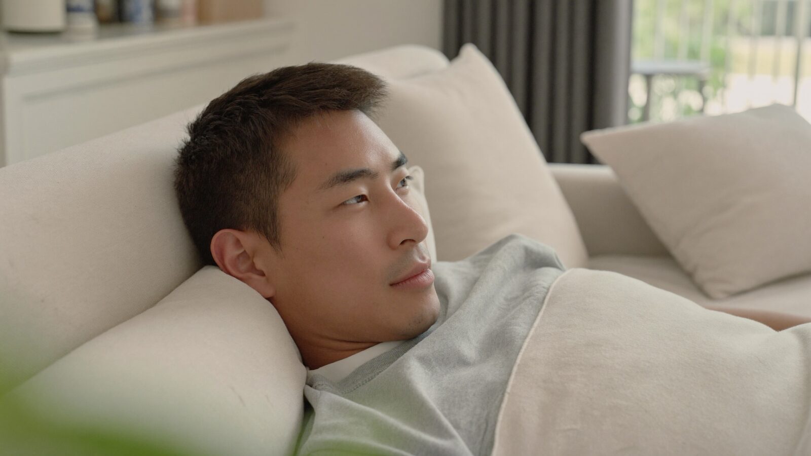 Man with short neat hair resting on a sofa under a light blanket