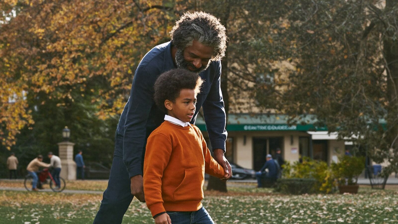 Man with full, curly gray hair walking with a young boy in an autumn park