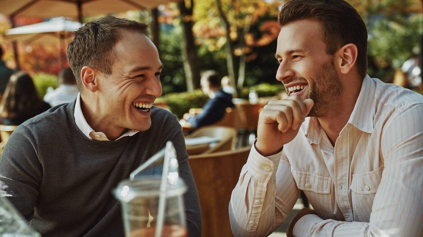 Two men laughing together at an outdoor cafe in autumn