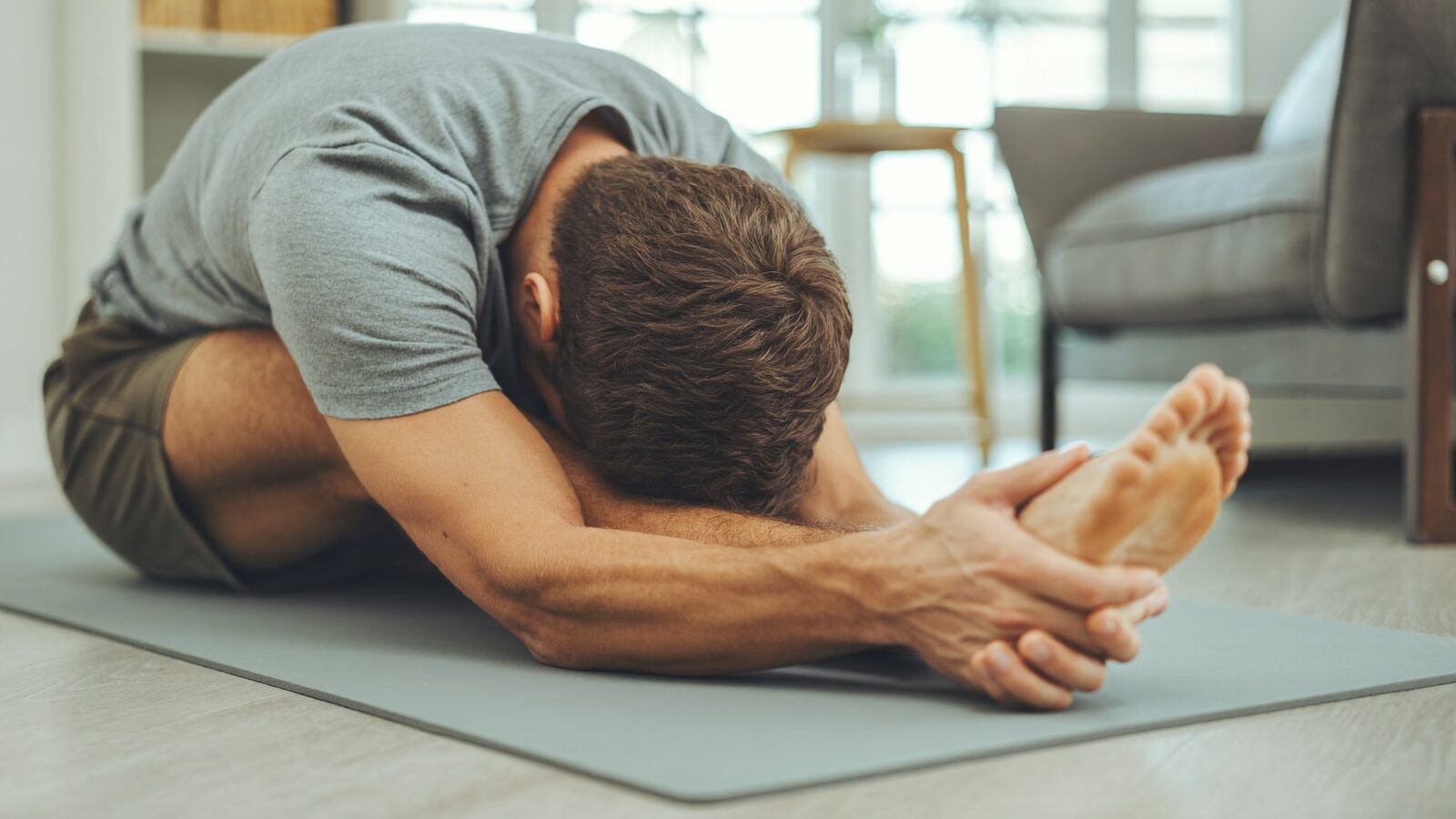 Man stretching on a yoga mat in a bright apartment